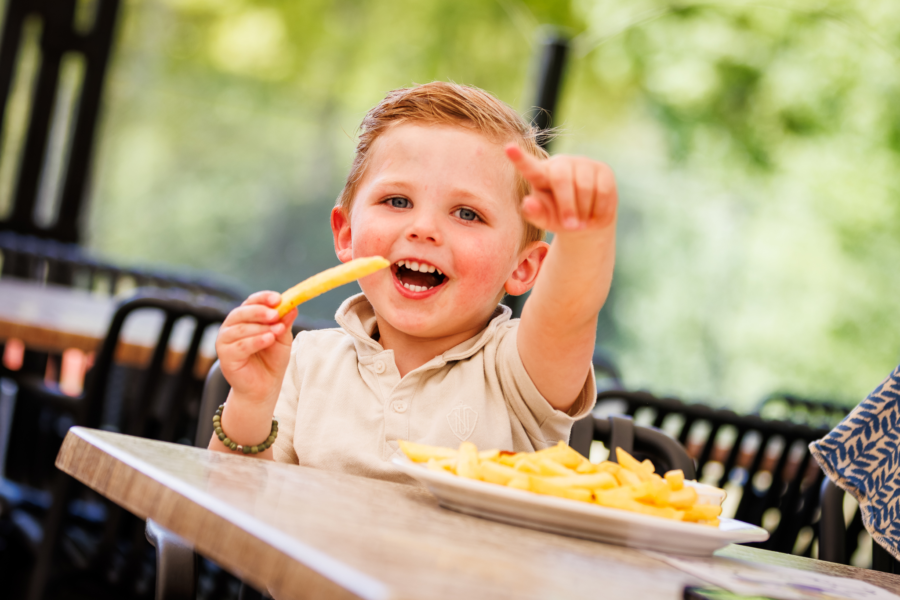 Jongen lacht met een bord patat op het terras